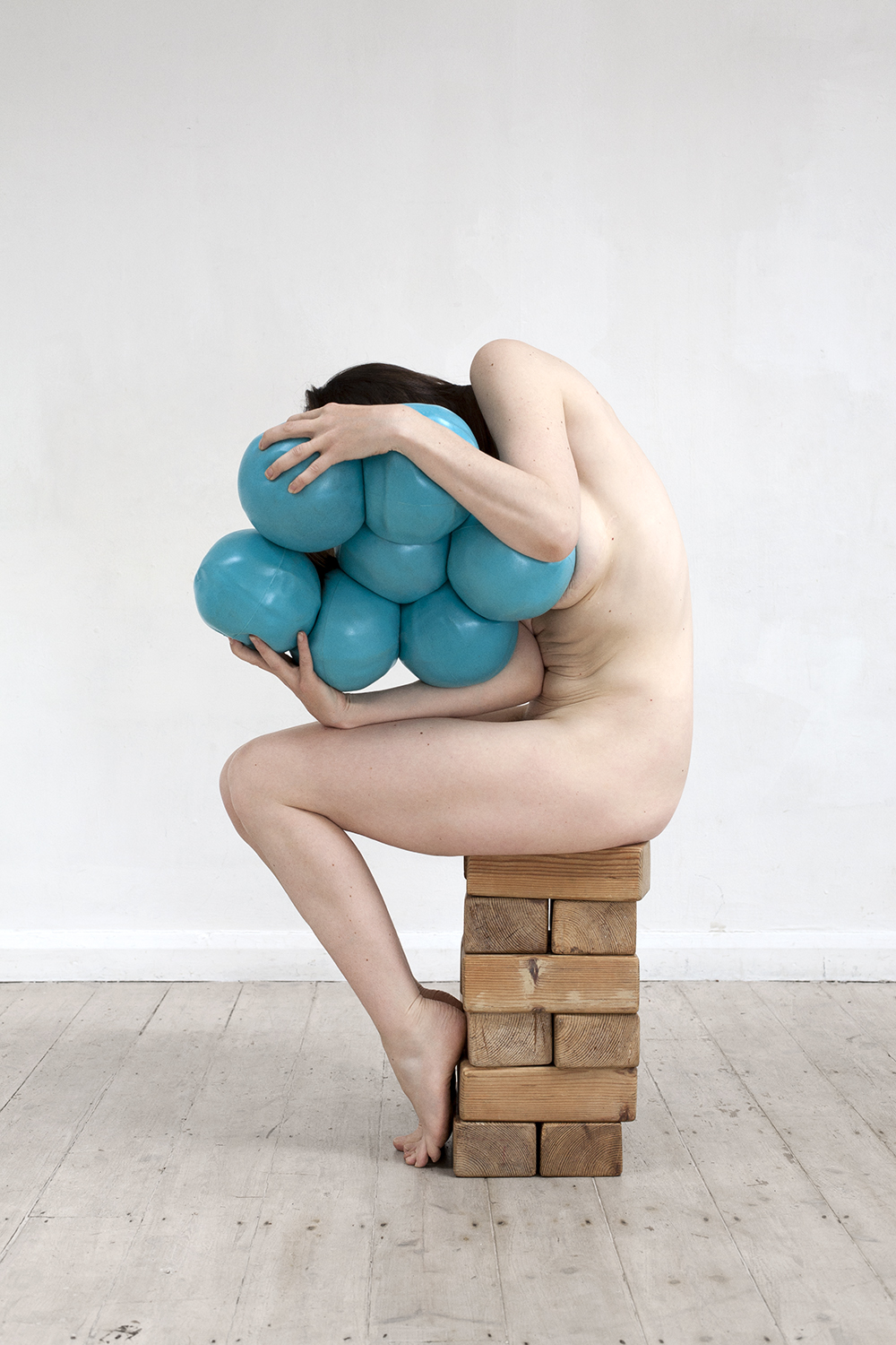 From the A Picture of Health exhibition, a naked woman clutches large squishy blue balls as she's sat on a stack of bricks hunched over