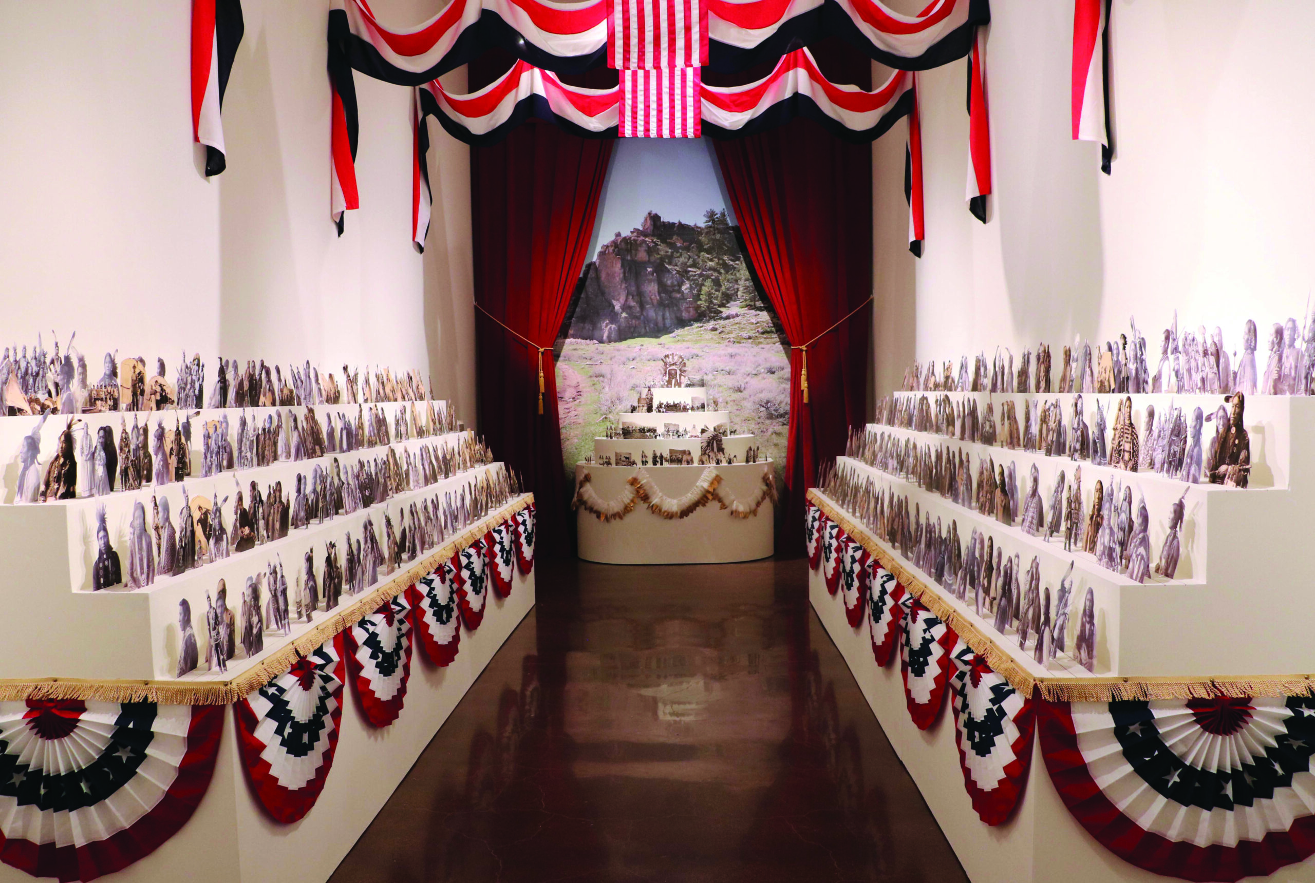 Part of Wendy Red Star's installation she is decolonizing the image with black and white images of Native Americans in rows above festive American banners of red, white and blue