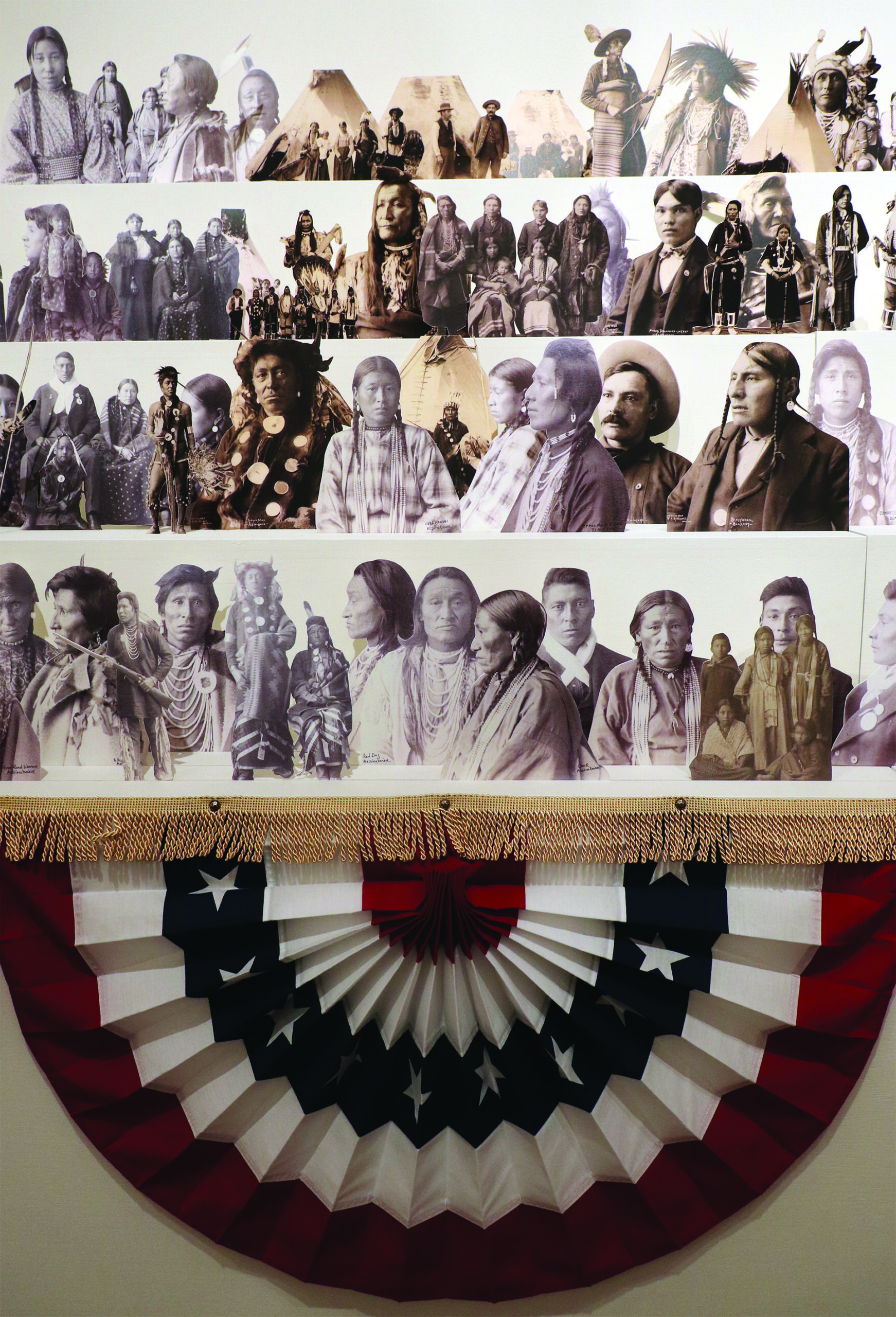 Part of Wendy Red Star's installation she is decolonizing the image with black and white images of Native Americans in rows above festive American banners of red, white and blue