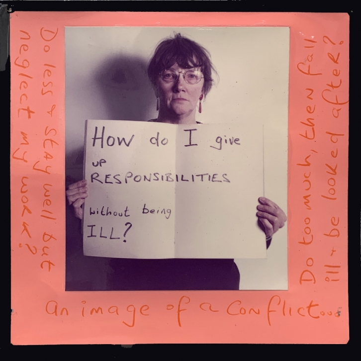 Jo Spence holds a handwritten sign which reads, 'How do I give up responsibilities without being ill?'