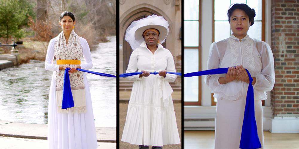 Three women wearing white dresses hold a blue sash