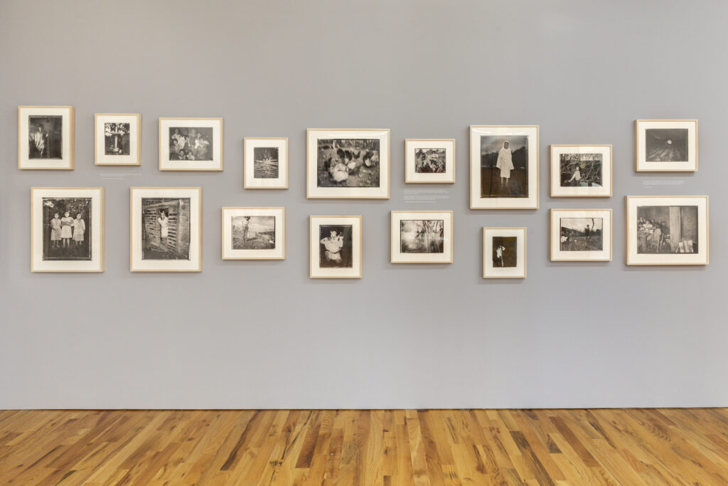 Installation image showing white frames, containing photographs by Wendy Ewald, displayed on a grey wall.