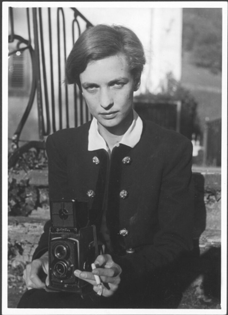 young woman with camera and cigarette looking straight into camera