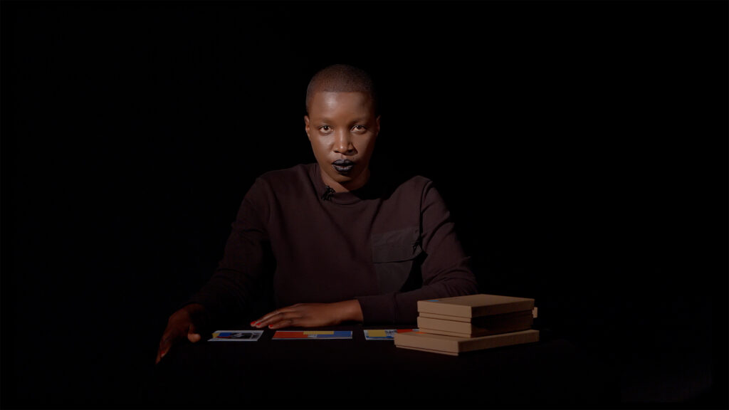 Portrait photograph showing Belinda Kazeem-Kamiński seated in front of a stack of books and art prints.
