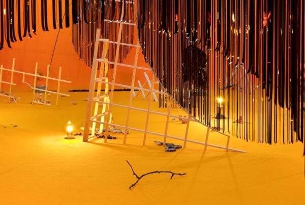 Installation image. A room bathed in orange light. A white metallic structure leans over in the centre of the image.