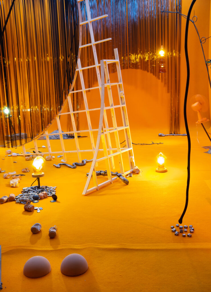 Installation image. A room bathed in orange light. A white metallic structure leans over in the centre of the image.