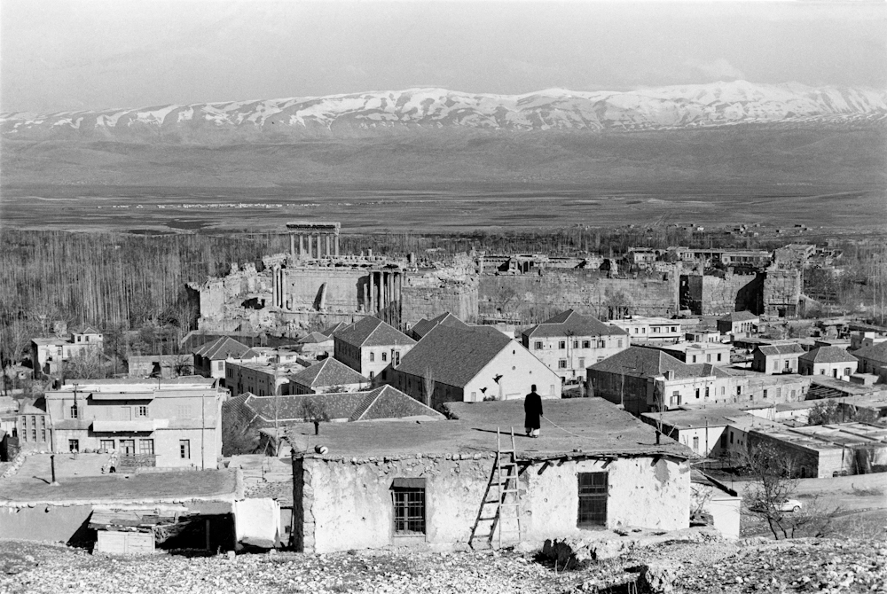 Black and white landscape image showing a village backed by a mountain range.