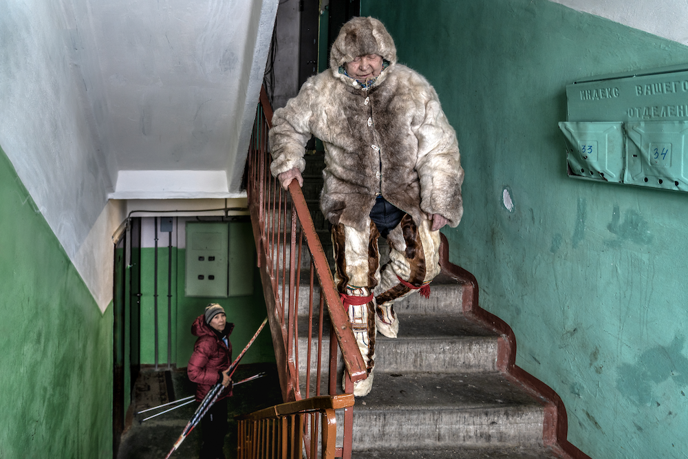 A Saami person descends a set of stairs while another person waits for them, slightly lower down in the left of the image.