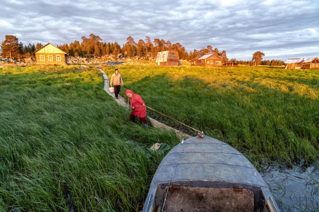 Two Saami villagers drag a boat across a field of grass.