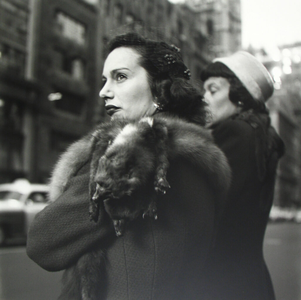 Candid black and white photo of two women wearing fur hooded coats.