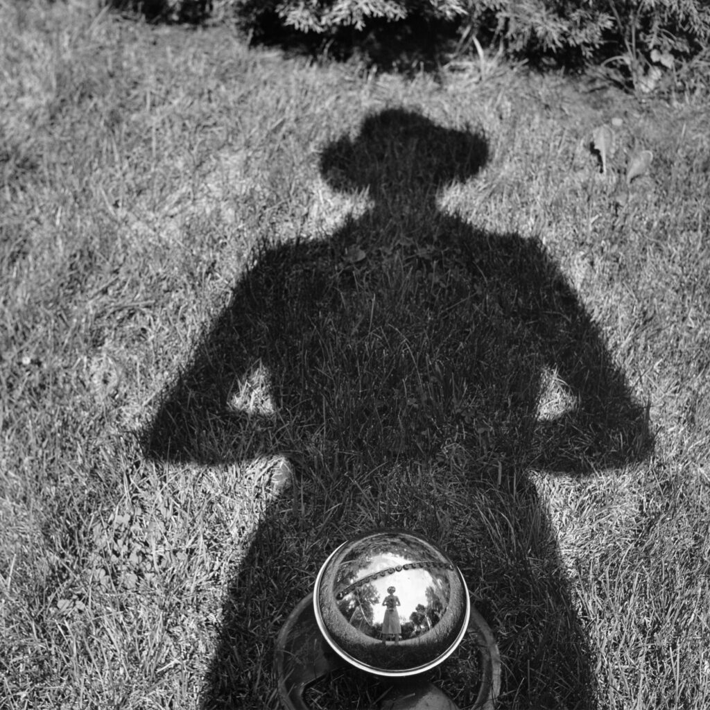 Black and white photo of Vivian Maier's shadow on a patch of grass.