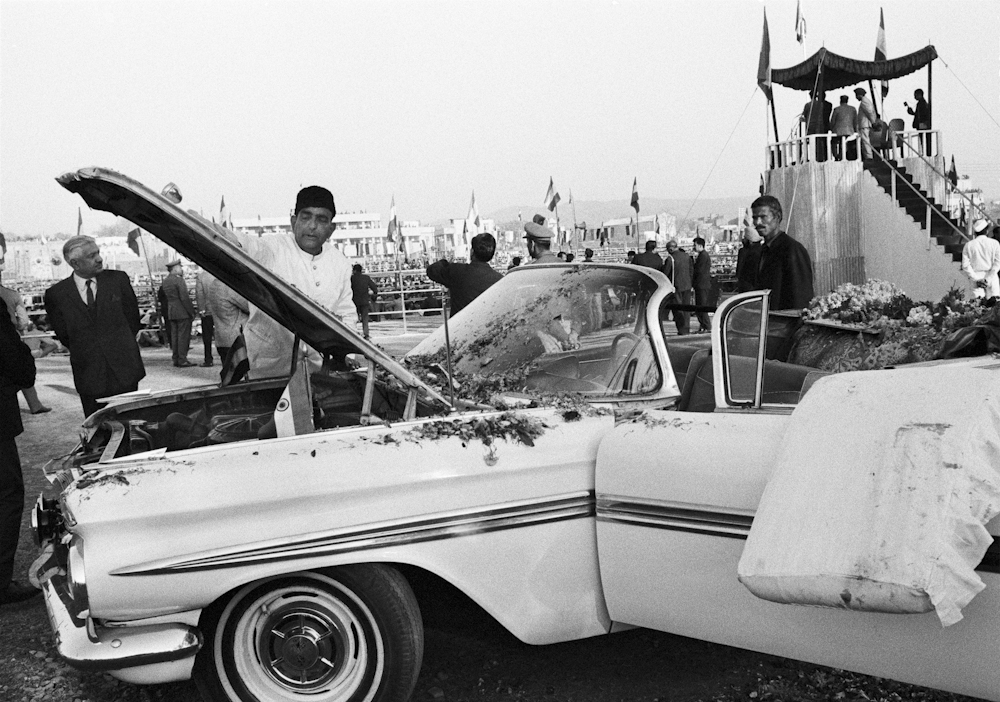 Black and white photo of Indira Gandhi's driver standing next to a car with an open hood.