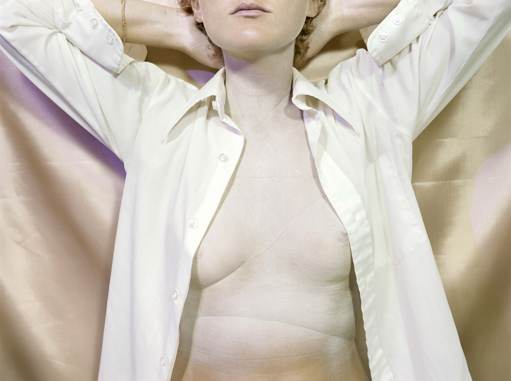 The torso of a woman, whose eyes and nose are cropped out of the top edge of the image. Her white shirt is unbuttoned.
