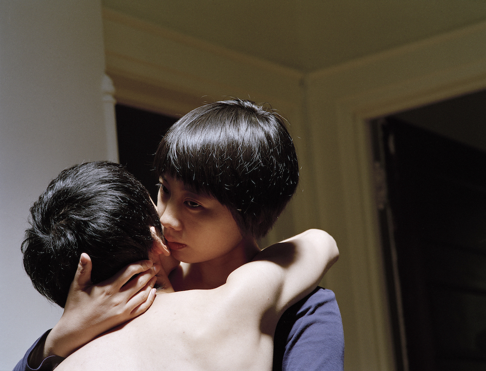 A woman (Pixy) faces towards the camera while embracing a man (Moro), who faces away. Pixy wears a navy blue shirt, Moro is shirtless. Only their head and shoulders is visible.