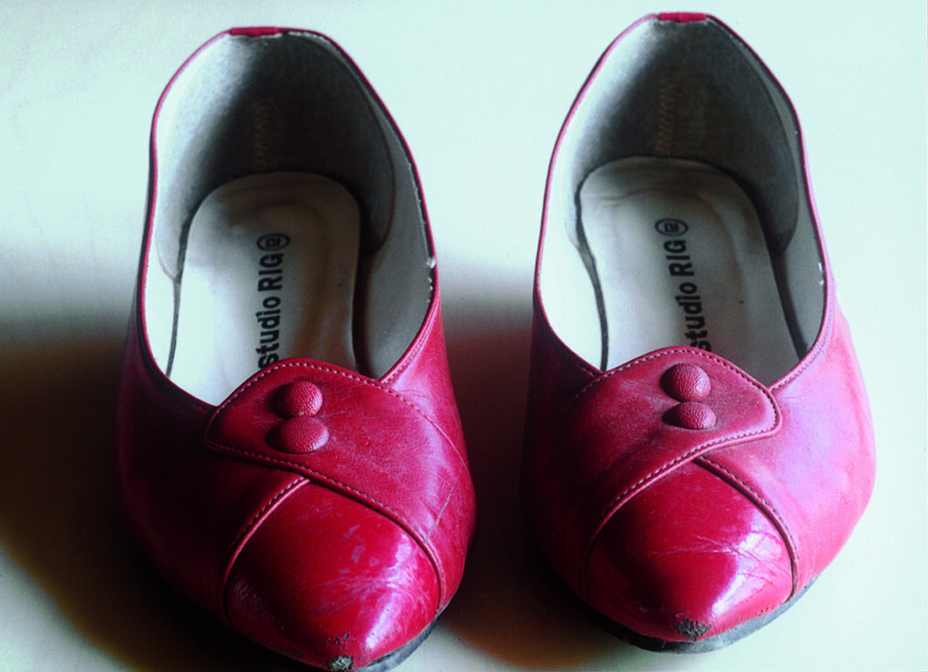 A pair of red shoes with slightly pointed toes. They are in used condition with some marks and blemishes.