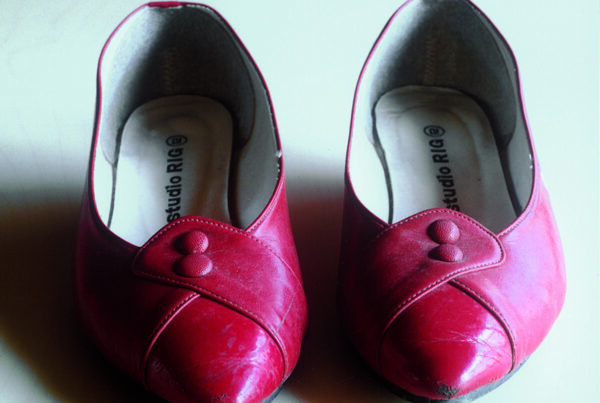 A pair of red shoes with slightly pointed toes. They are in used condition with some marks and blemishes.