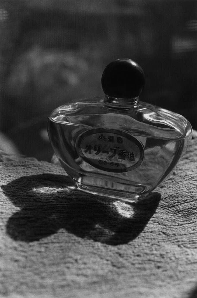 Black and white image of a small glass perfume bottle. The stopper is spherical and opaque.