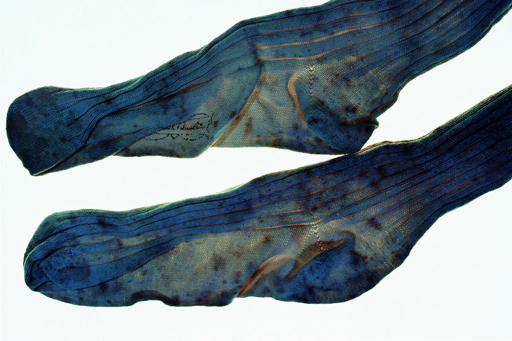 A stained pair of blue socks with light showing through; one has a small black symbol on it.