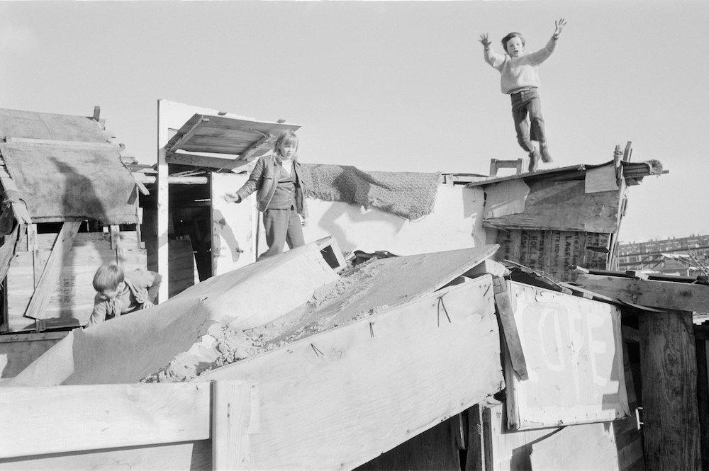 Black and white photo of three children climbing atop their hand-built wooden structures.
