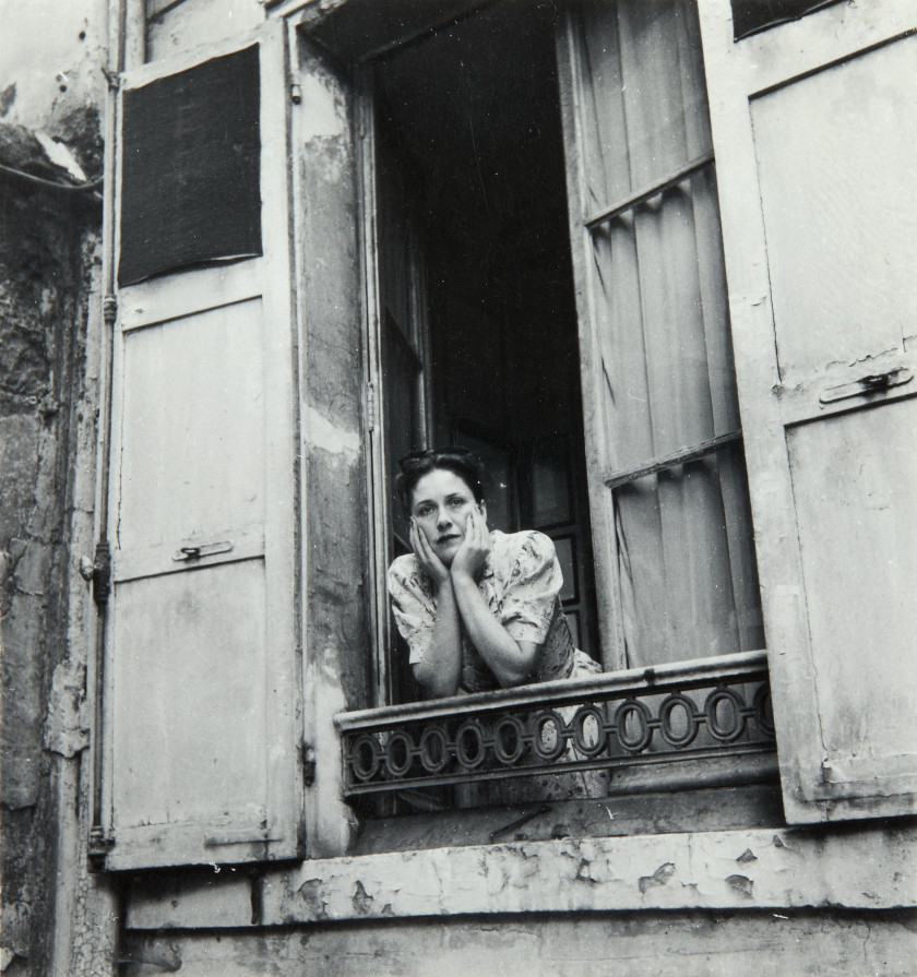 Black and white image of a woman (Dora Maar) leaning out of a window. Her head rests upon her hands.
