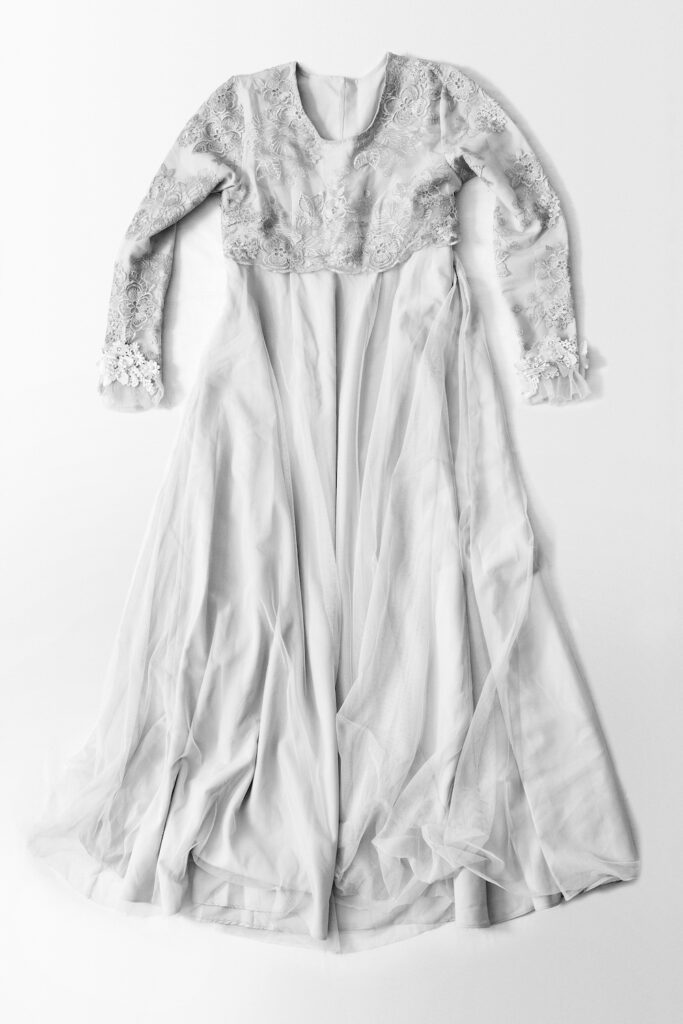 Black and white photograph of a long sleeved wedding dress with lace detail on the chest and arms.