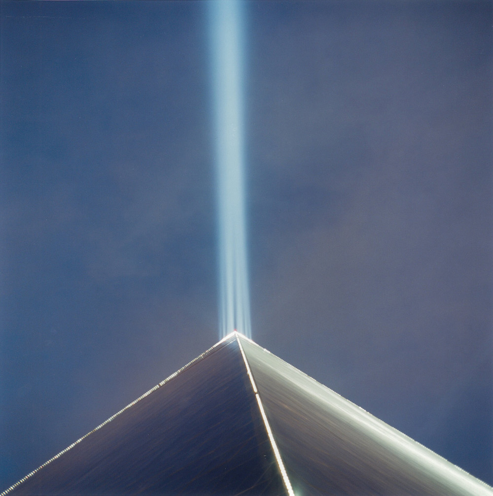 Colour photograph depicting a ray of blue light emerging from the point of a glass prism.