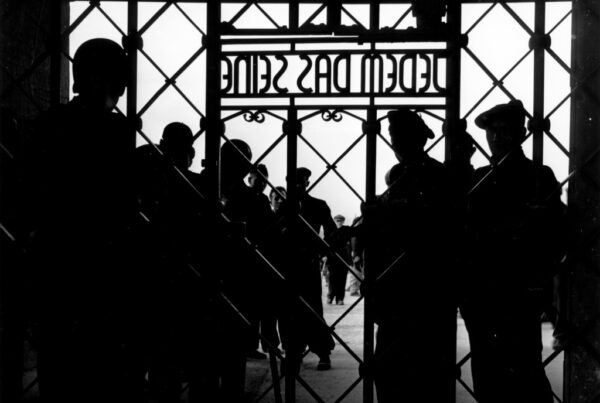 Black and white photograph. Silhouettes of people standing behind the gate of a concentration camp, Buchenwald.