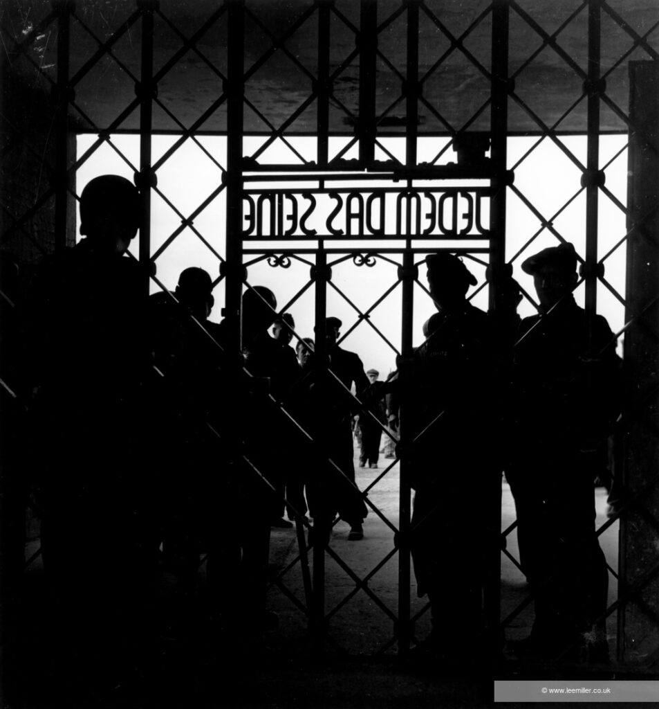 Black and white photograph. Silhouettes of people standing behind the gate of a concentration camp, Buchenwald.