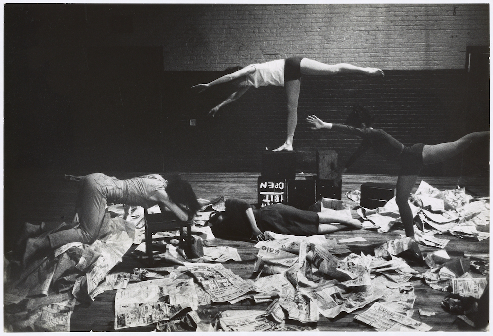 Black and white photograph. Dancers surrounded by piles of newspaper.