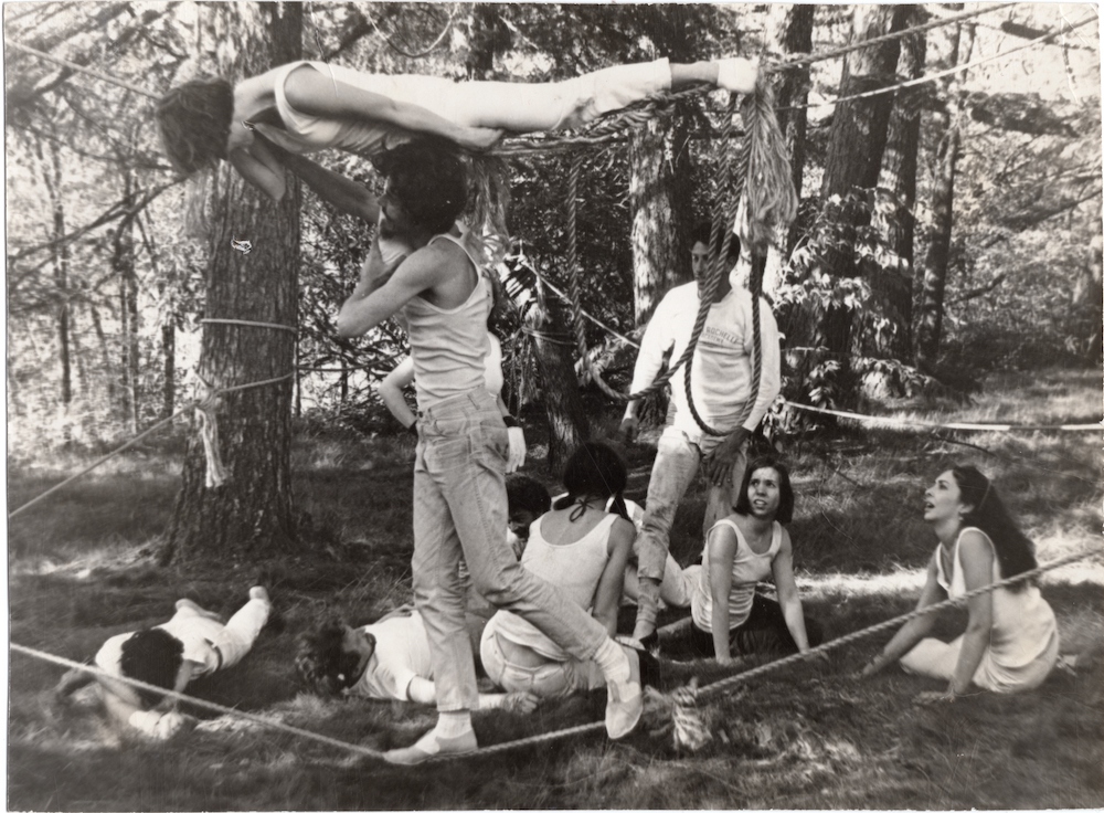 Black and white photograph showing a dance in performance. The dancers are dressed in white and surrounded by ropes.