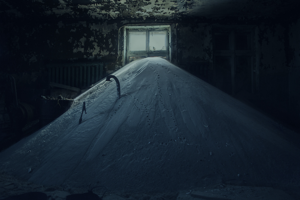 Colour photograph from Hyperborea. A dark interior setting. A mound of snow partially obscures a window. It is covered in small holes, perhaps footprints left by a small bird or mammal.