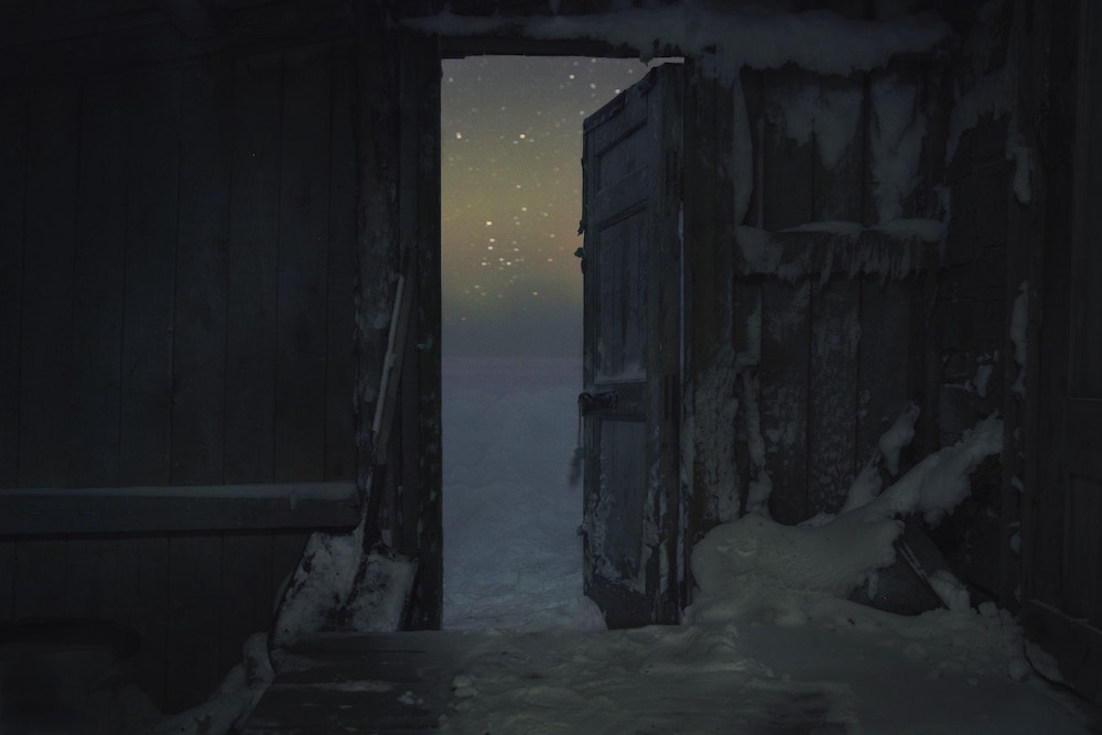 Colour photograph. Stars shine in the night's sky, viewed through a wooden doorway covered in snow.