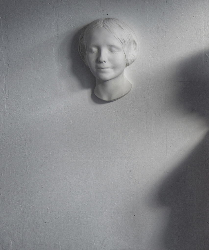 The plaster cast mask of the famous L’INCONNUE DE LA SEINE is displayed on a white wall.