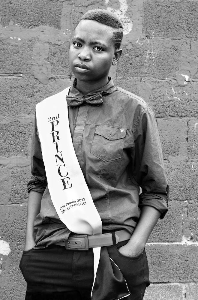 Black and white photograph. The subject wears a sash with the words '2nd Prince 2012 - Mr Uthingo'' printed on it.