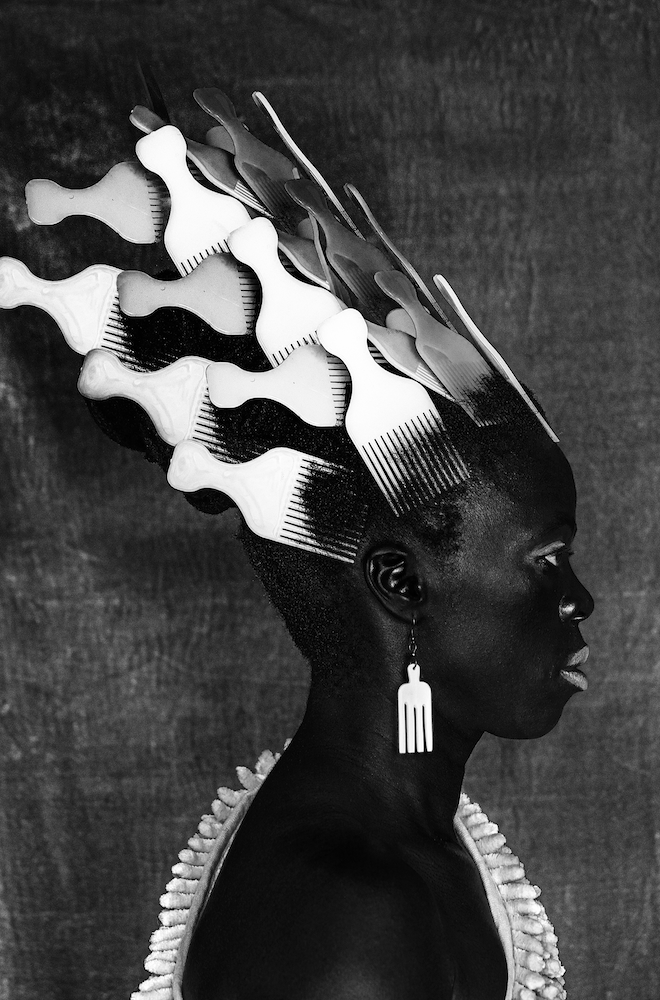 Black and white photograph. Zanele in profile, facing right, with a tall arrangement of combs in their hair.
