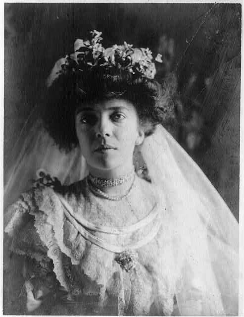 Black and white photo of a woman (Alice Roosevelt) in a wedding dress. She also wears a veil, while hangs at the back of her head.