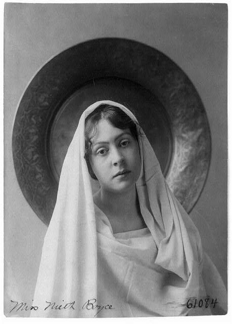 Black and white photograph. A woman wears a white shawl and headscarf.