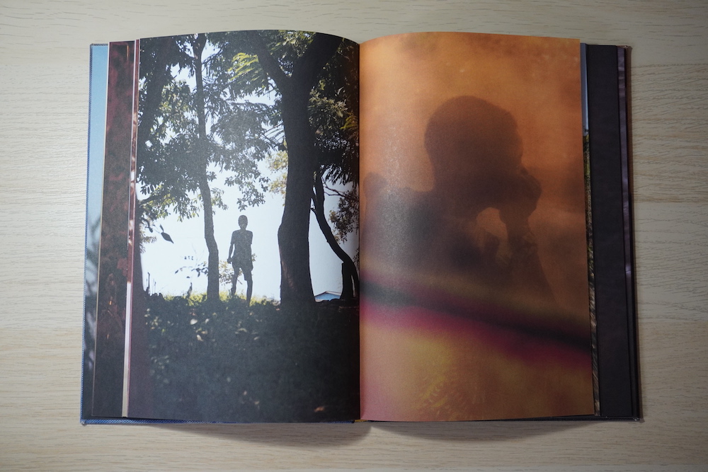 Double page spread showing colour photographs of a person coming over a hill, silhouetted, and a person in profile, shrouded by an orange haze.