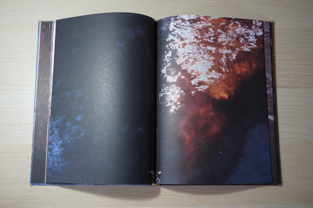Double page spread. The photograph depicts the surface of water; on the right side of the image we see streaks of sunlight reflected.