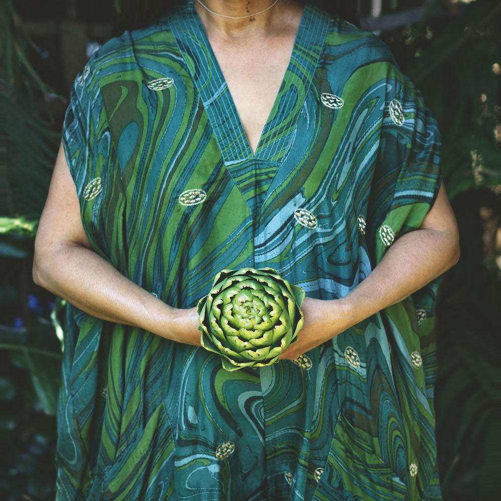 Colour photograph. A person in a blue and green dress holds an artichoke.