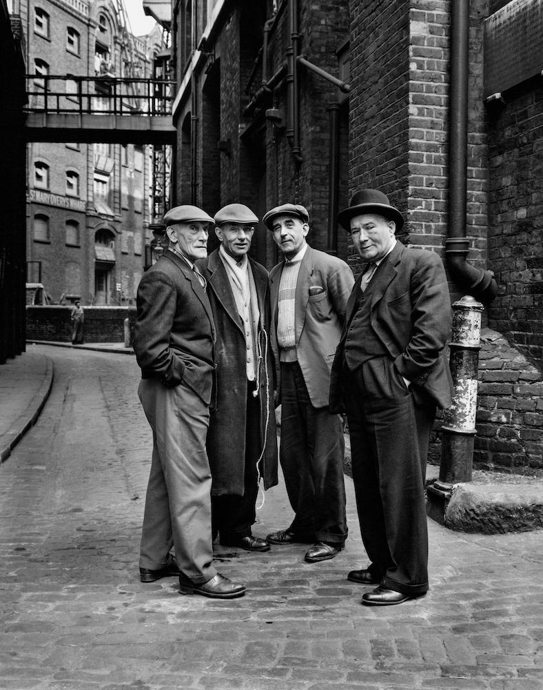 Black and white photograph. Four men standing in the street.