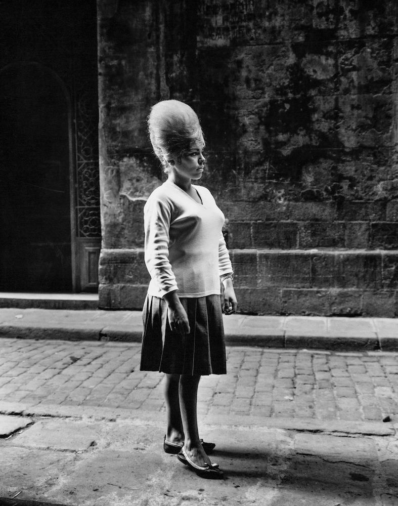 Black and white photograph of a woman standing in a cobbled street.