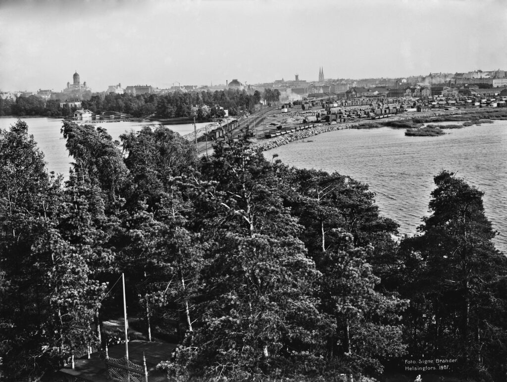 Black and white photo showing a copse of trees and a city (Helsinki) from an aerial view.
