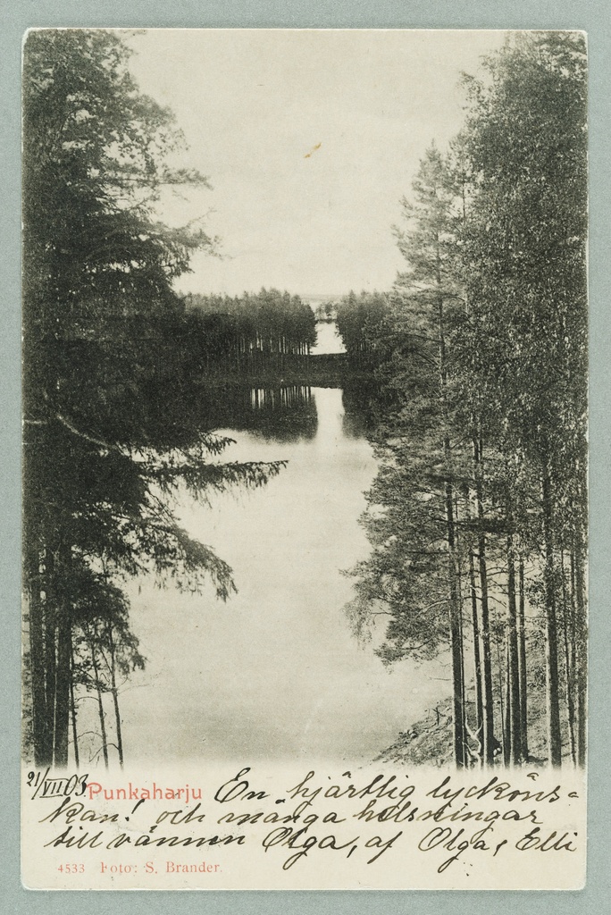 Black and white photo of a lake surrounded by trees. There are annotations beneath the image in a cursive script.