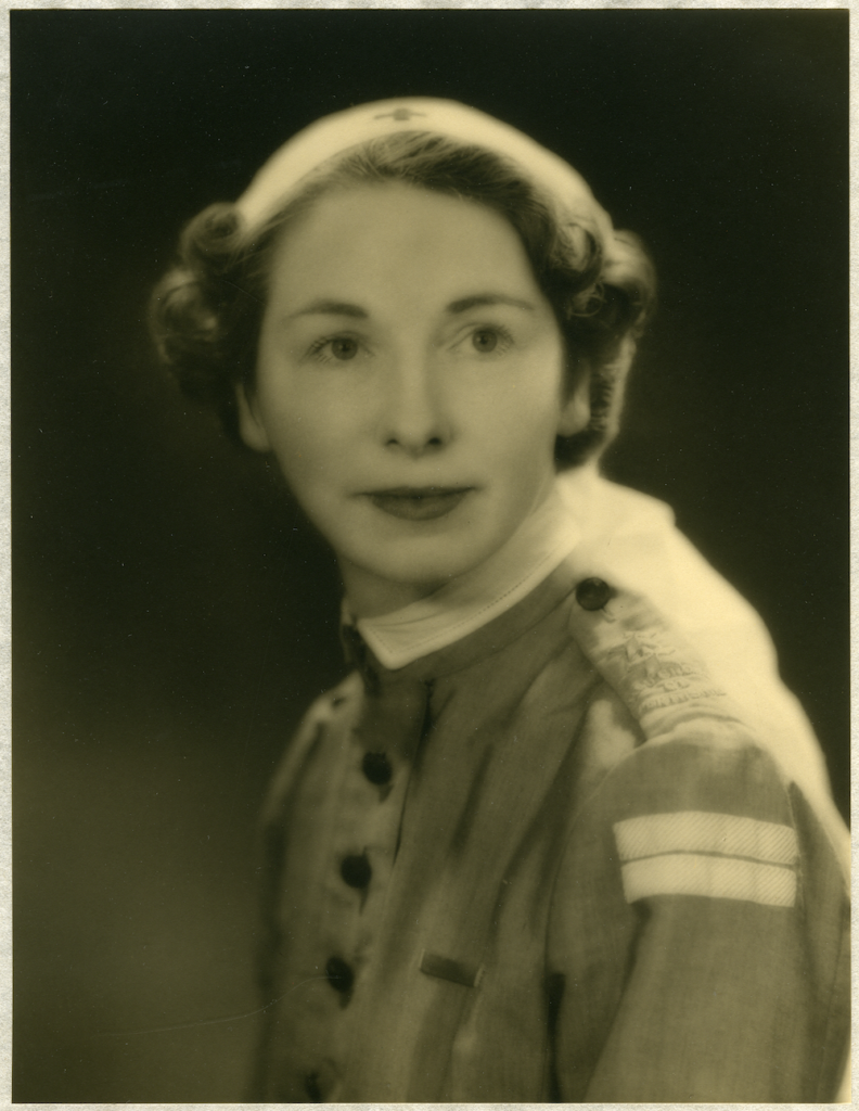 A black and white portrait photograph of a woman, Margaret, wearing a 1940s nurse uniform. She has short, slightly curled hair and wears a buttoned up shirt with a stiff collar and two small stripes on the shoulder.