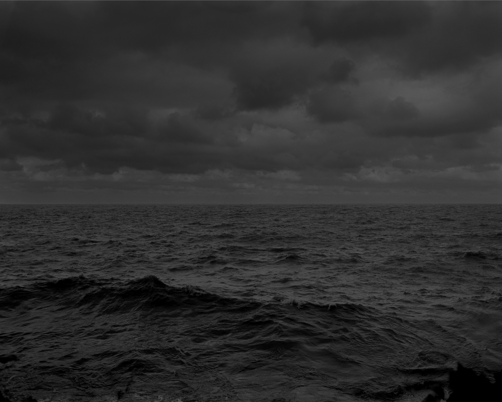 A landscape photograph of a darkly coloured sea, overcast with dark clouds.