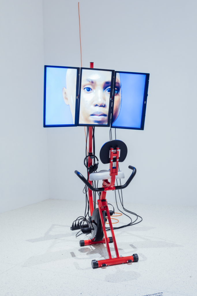 An exercise machine is arranged in front of three screens depicting a human face.