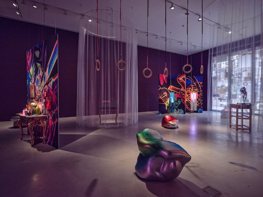 Installation view showing hanging rings and curtains, as well as abstract sculptural forms with glittery surfaces.