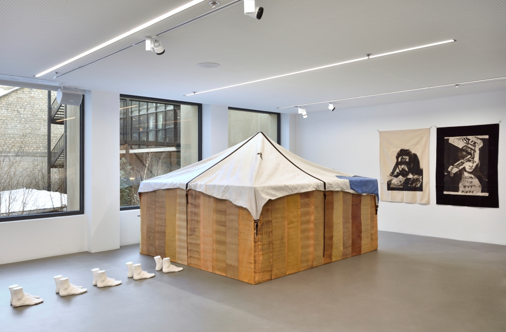 View of the exhibition The Earth has Shifted, Ab-Anbar Gallery at L'Atlas. A tent is pictured in the centre of a room, with pairs of ceramic feet approaching it.
